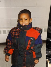 a young boy in a plaid jacket standing next to a bag