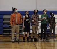 a group of people standing on a basketball court with masks on